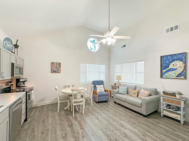 living area featuring high vaulted ceiling, light wood-type flooring, visible vents, and a ceiling fan