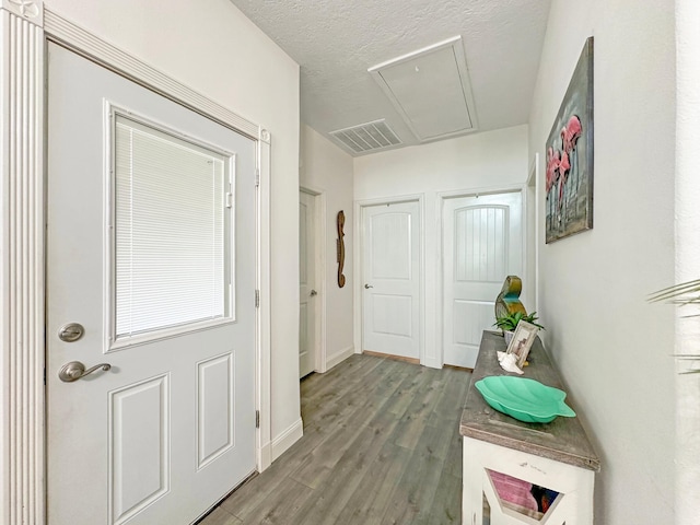 doorway featuring a textured ceiling, wood finished floors, visible vents, and baseboards