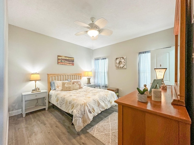 bedroom featuring ceiling fan, a textured ceiling, baseboards, and wood finished floors