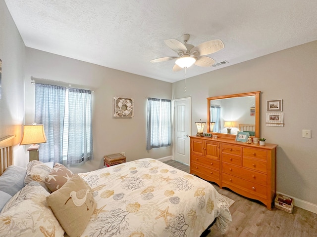 bedroom featuring baseboards, visible vents, a ceiling fan, wood finished floors, and a textured ceiling