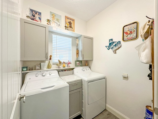 clothes washing area with cabinet space, baseboards, a textured ceiling, light wood-type flooring, and washing machine and dryer