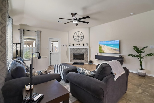 living room with a ceiling fan, baseboards, vaulted ceiling, and a tiled fireplace