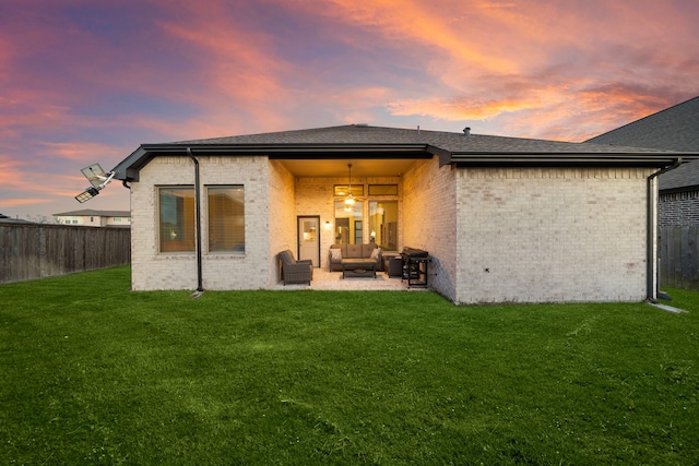 back of property at dusk featuring a fenced backyard, brick siding, outdoor lounge area, a yard, and a patio area