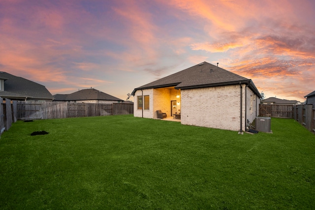 back of house at dusk featuring brick siding, a fenced backyard, cooling unit, and a yard