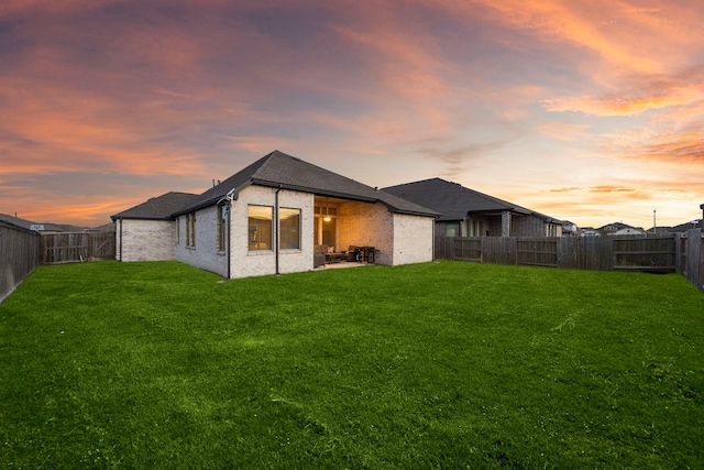 back of house featuring brick siding, a fenced backyard, a patio area, and a yard