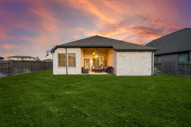 back of property with a shingled roof, a patio, a fenced backyard, a yard, and brick siding