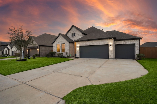 french country inspired facade featuring a garage, roof with shingles, a lawn, and concrete driveway