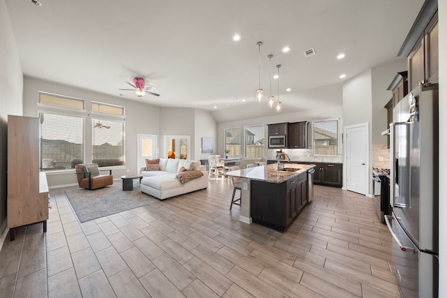 kitchen featuring a breakfast bar area, stainless steel appliances, visible vents, open floor plan, and a sink