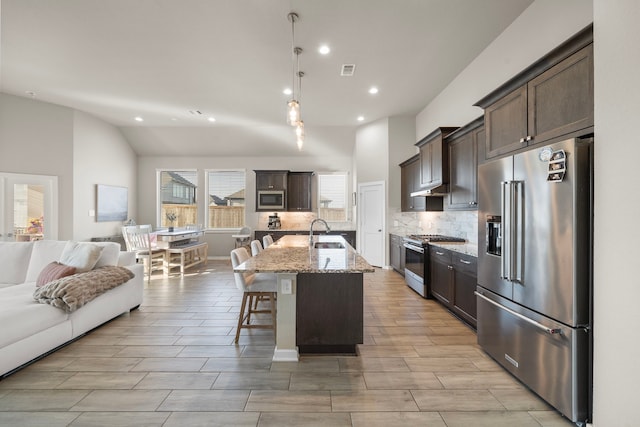 kitchen with open floor plan, stainless steel appliances, dark brown cabinets, and a sink