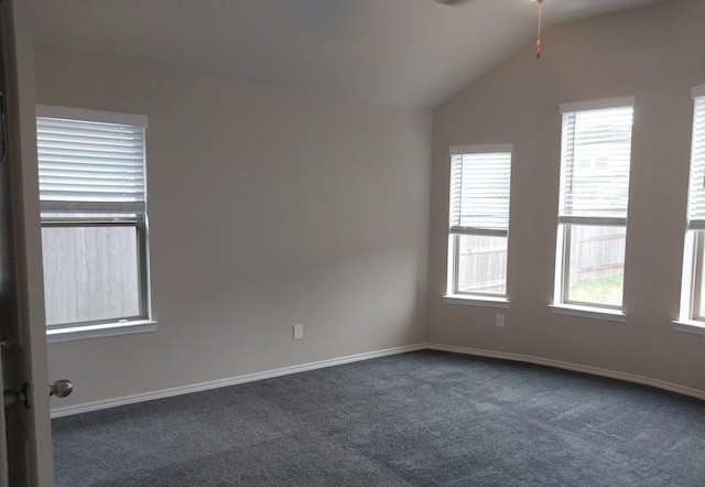 empty room with dark colored carpet, a healthy amount of sunlight, vaulted ceiling, and baseboards