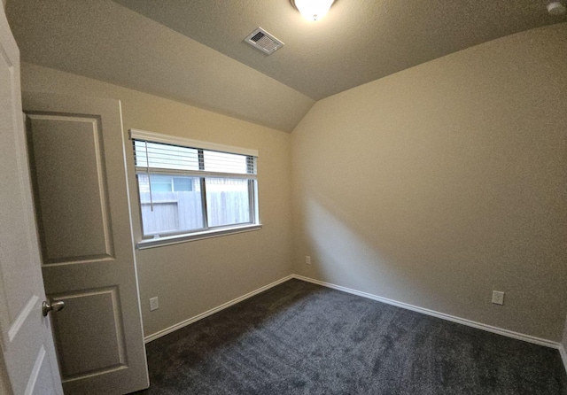 unfurnished room featuring vaulted ceiling, dark colored carpet, visible vents, and baseboards