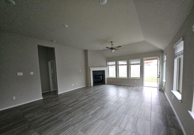 unfurnished living room featuring lofted ceiling, dark tile patterned flooring, a fireplace, a ceiling fan, and baseboards