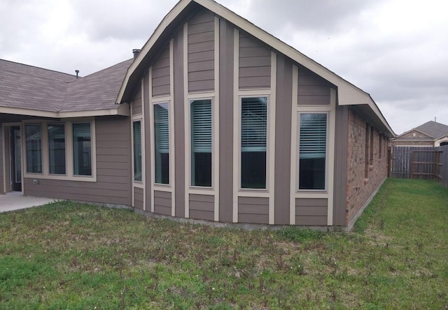 view of side of property with a shingled roof, a yard, and fence