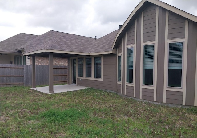 back of house featuring a yard, a shingled roof, fence, and a patio