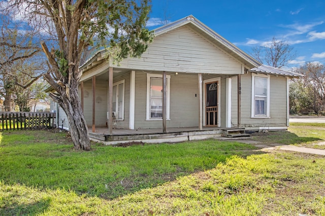 view of front of property with a front yard, covered porch, fence, and metal roof