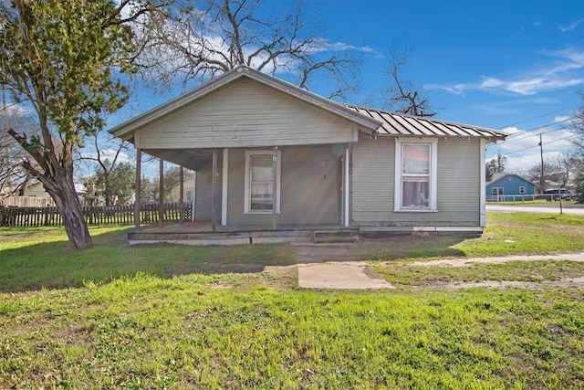 bungalow-style house featuring a porch, a front yard, a standing seam roof, fence, and metal roof