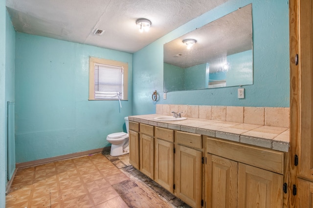 bathroom featuring toilet, vanity, a textured ceiling, baseboards, and tile patterned floors