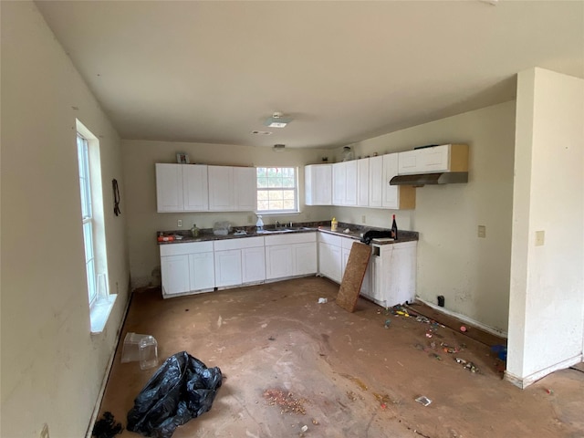 kitchen with dark countertops, white cabinets, a sink, concrete floors, and under cabinet range hood