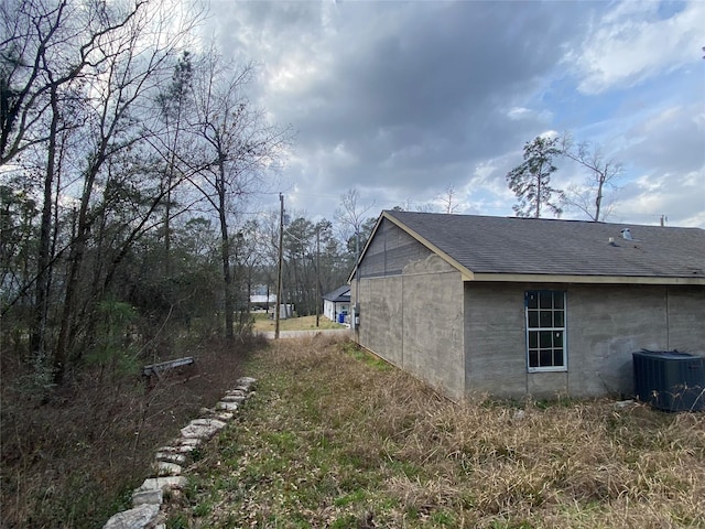 view of side of property featuring central AC unit and roof with shingles