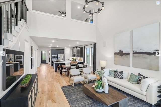 living room featuring ceiling fan with notable chandelier, stairway, and light wood-type flooring