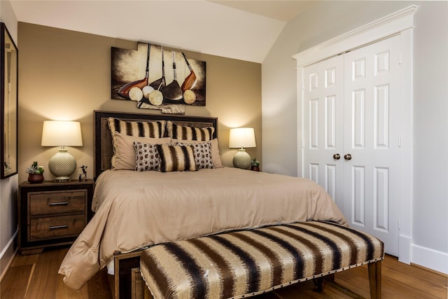 bedroom featuring lofted ceiling, a closet, wood finished floors, and baseboards