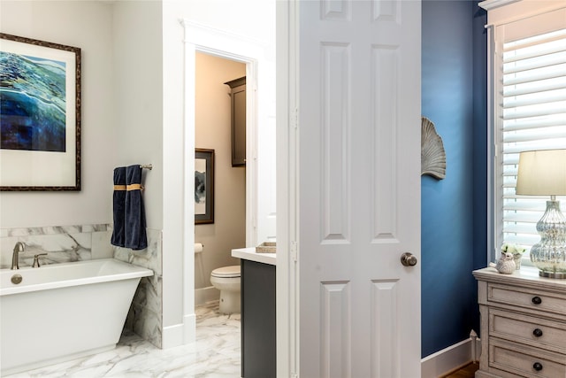 full bath featuring toilet, vanity, baseboards, a freestanding bath, and marble finish floor