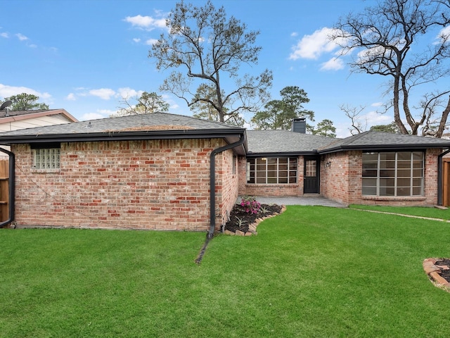 rear view of house with brick siding, a lawn, a chimney, and a shingled roof