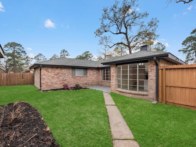 back of house with a lawn, a fenced backyard, a shingled roof, brick siding, and a chimney