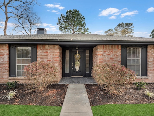 property entrance featuring a shingled roof, brick siding, and a chimney