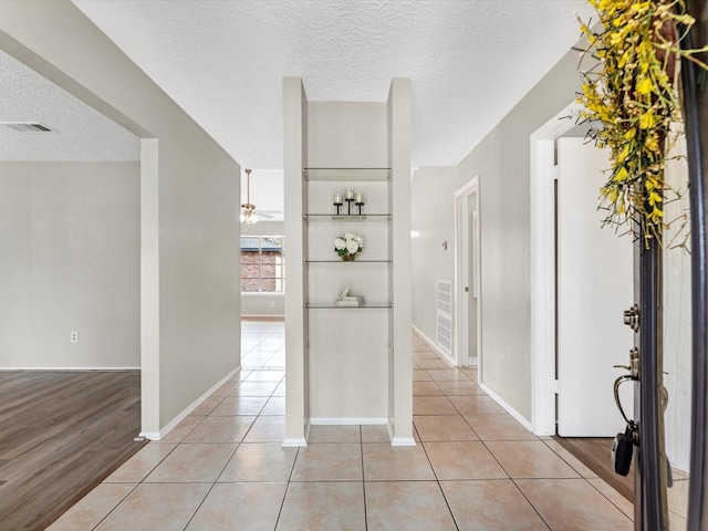 hall with visible vents, baseboards, a textured ceiling, and light tile patterned flooring