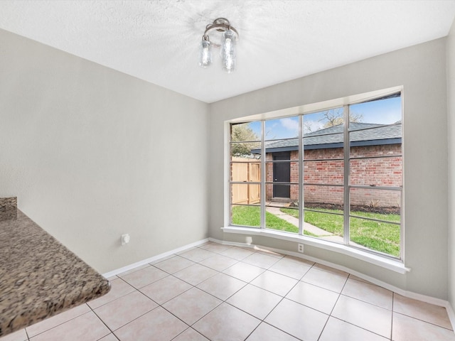 unfurnished dining area featuring light tile patterned flooring, baseboards, and a textured ceiling