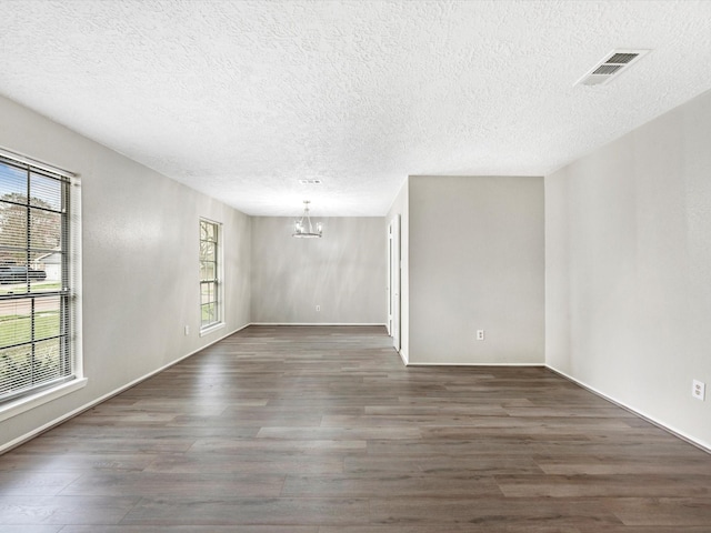 empty room featuring visible vents, wood finished floors, a textured ceiling, and a chandelier