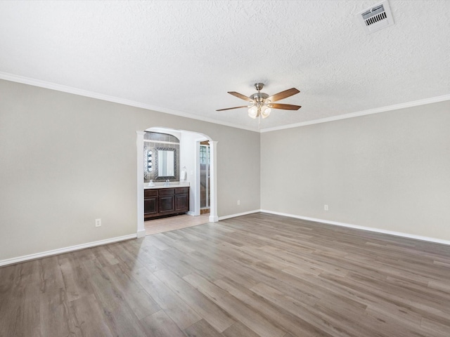 unfurnished living room featuring visible vents, crown molding, baseboards, light wood-style floors, and arched walkways