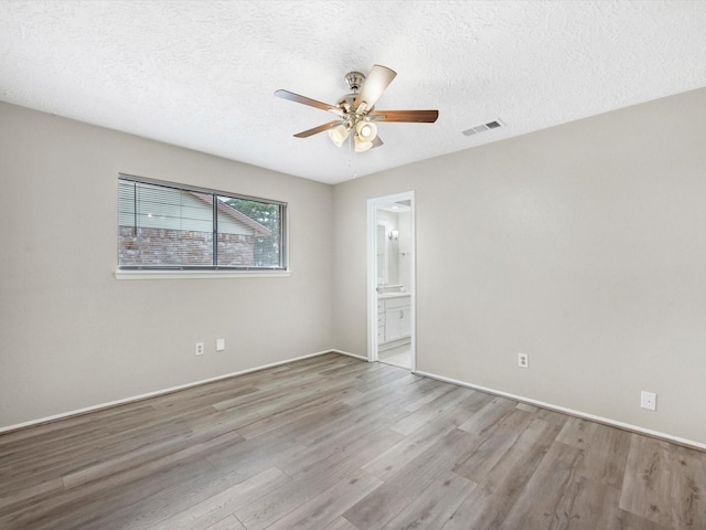 spare room featuring a ceiling fan, baseboards, wood finished floors, visible vents, and a textured ceiling