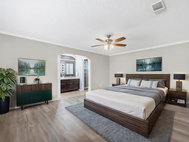 bedroom with crown molding, light wood-style flooring, arched walkways, and visible vents