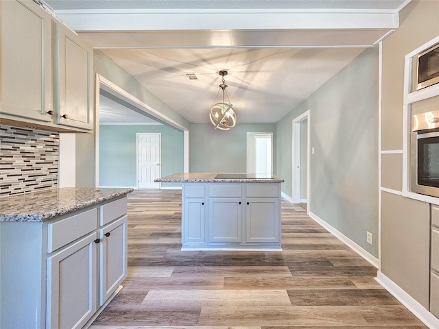 kitchen featuring wall oven, baseboards, backsplash, light wood finished floors, and stainless steel microwave