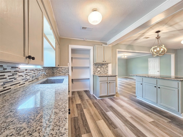 kitchen with light wood finished floors, tasteful backsplash, light stone countertops, pendant lighting, and a sink