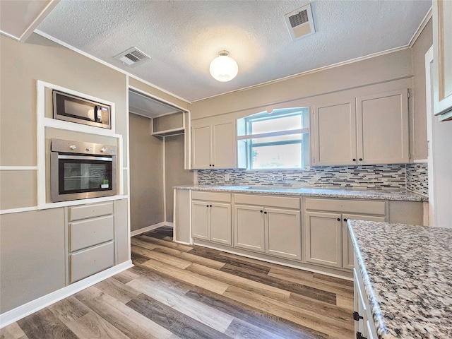 kitchen with light wood-type flooring, visible vents, stainless steel appliances, and backsplash