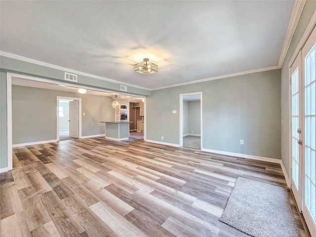 empty room with light wood finished floors, baseboards, visible vents, ornamental molding, and a textured ceiling