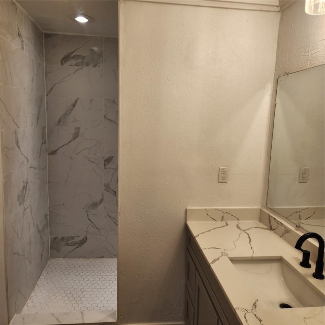 bathroom with a textured wall, a marble finish shower, and vanity