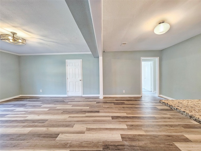 unfurnished room with a textured ceiling, baseboards, wood finished floors, and ornamental molding