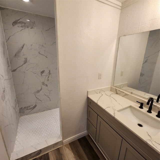 full bathroom with a textured wall, vanity, wood finished floors, tiled shower, and baseboards