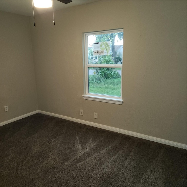 empty room featuring ceiling fan, dark colored carpet, a wealth of natural light, and baseboards