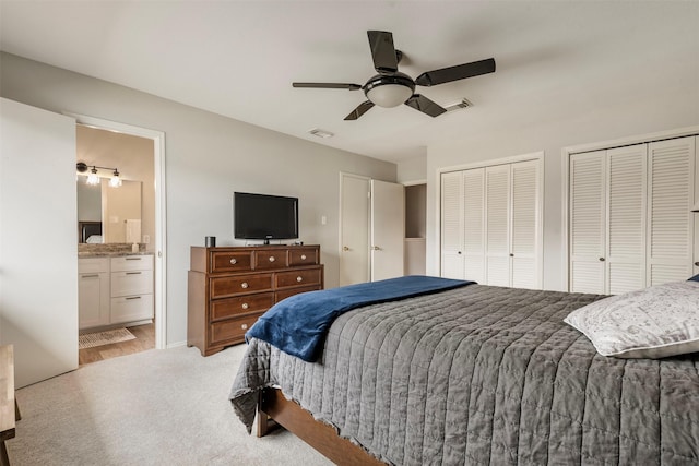 bedroom featuring light carpet, visible vents, multiple closets, and ensuite bathroom