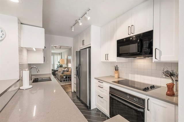 kitchen featuring light stone counters, a sink, white cabinetry, black appliances, and tasteful backsplash