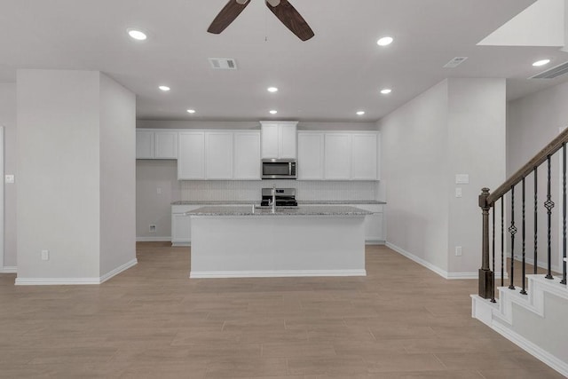 kitchen featuring stainless steel appliances, visible vents, white cabinets, light wood-type flooring, and a center island with sink