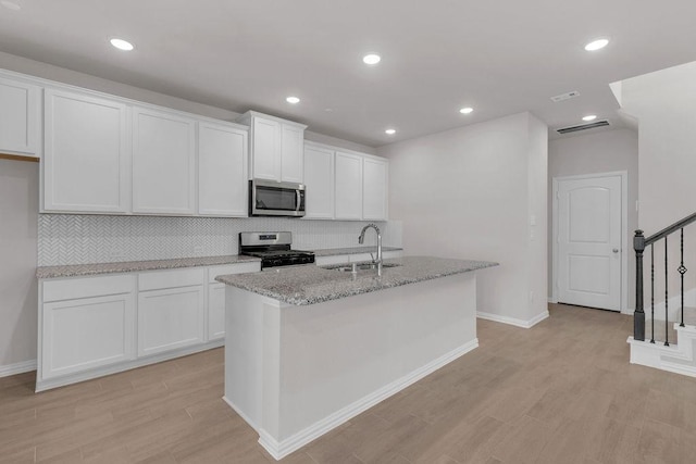 kitchen with stainless steel appliances, white cabinets, a sink, light stone countertops, and light wood-type flooring