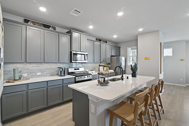 kitchen featuring a center island with sink, visible vents, gray cabinetry, appliances with stainless steel finishes, and a kitchen breakfast bar