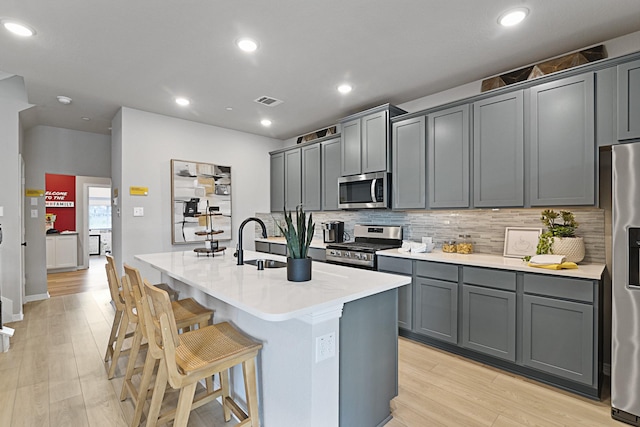 kitchen with a sink, light wood-style floors, a kitchen breakfast bar, appliances with stainless steel finishes, and a center island with sink