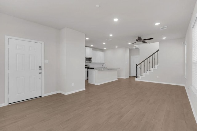 unfurnished living room with recessed lighting, visible vents, light wood-style flooring, stairway, and ceiling fan